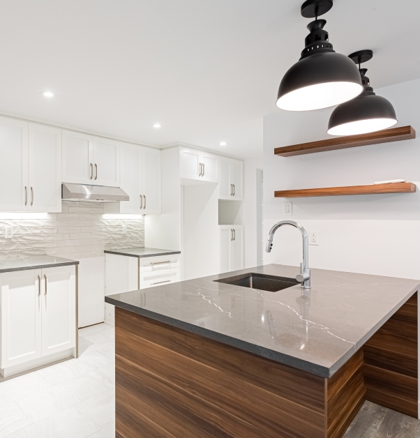 Modern white kitchen with white cabinets and white ceramic backsplash, central kitchen island with grey quartz countertops, brown shelves and white ceramic floor.