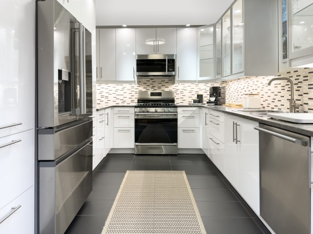 Modern U-shaped layout kitchen with white cabinets, some with glass doors, stainless steel appliances and 3-colour backsplash