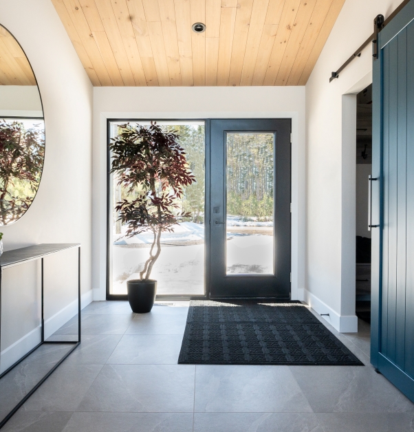 Bright, white hallway in a modern house, large windows, cerulean blue door, mudroom, ceiling with natural wood slats and gray ceramic floor.