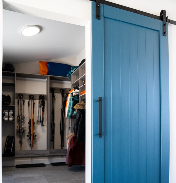 Cerulean blue sliding door, white mudroom entrance with grey ceramic floor, various sports equipment and accessories, winter coats.