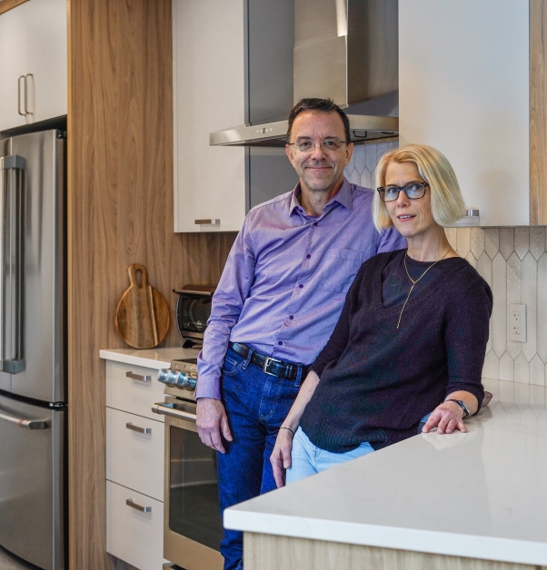 Couple in their modern renovated white kitchen with willow-gray and gold laminate cabinets and white ceramic backsplash.
