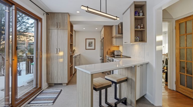 Modern white kitchen with laminate cabinets and white ceramic backsplash, white stone countertop, corner island and gray ceramic floor.